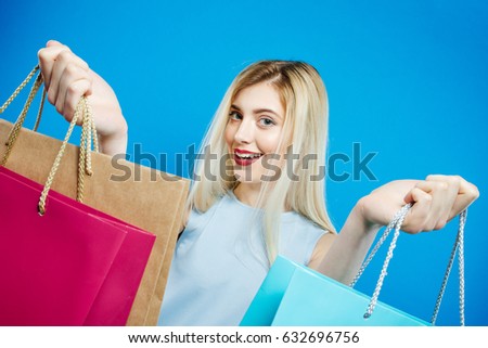Blonde with Wild Smile Holding a Lot of Shopping Colorful Bags. Happy Girl with Lond Hair and Charming Smile on Blue Background in Studio.
