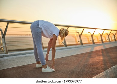 Blonde woman in activewear doing a standing forward bend on the bridge in the evening