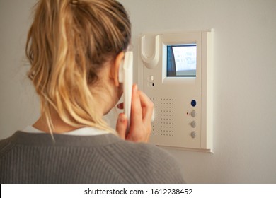 Blonde Woman Answering A Call At A Door Phone While Looking At The Screen On The CRT Display. Video Intercom Equipment. Selective Focus Image.