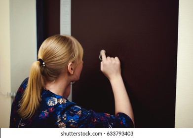 blonde woman answers the intercom call, hold the phone to his ear, waiting for the arrival of the long-awaited guest. Being in apartment near front door - Powered by Shutterstock