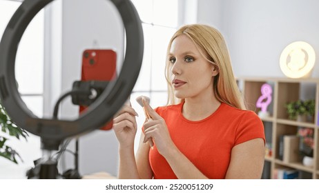 A blonde woman applies lipstick indoors using a ring light for a beauty tutorial in a well-lit studio. - Powered by Shutterstock