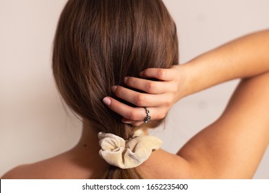 Blonde Woman With Beige Scrunchie On Her Ponytail, Holding It With Her Hand, Rose Ring On Her Finger. View From The Back.