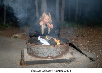 Blonde Woman Blows On A Campfire To Stoke The Fire And Flames At A Campground. Lots Of Smoke In The Air