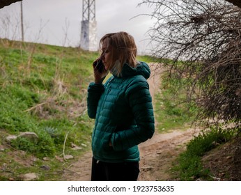 blonde woman with blue eyes, in a green winter coat, touching on the cell phone in a tunnel under a road crossing - Shutterstock ID 1923753635