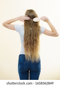 Blonde woman with brush combing her very long hair. Teenage girl with bad hair care. Back view