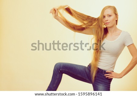 Blonde woman with brush combing her very long hair. Teenage girl taking care refreshing her hairstyle. Haircare concept.