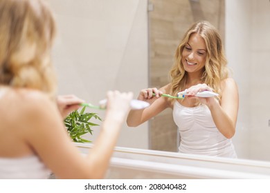 Blonde Woman Brushing Teeth In Front Of Mirror 