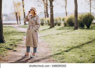 Blonde woman in coat outside in park using phone