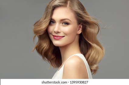Blonde woman with curly beautiful hair  on gray background. The girl with a pleasant smile. Short haircut . Bob hairstyle
