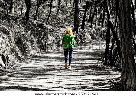 Blonde woman with curly hair walking on the path of trees and leaves in autumn in Montseny Natural Park in Barcelona, ​​Spain. Black and white effect