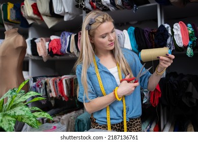 A blonde woman cuts a piece of thread from a bobbin. Tailor's workshop. - Shutterstock ID 2187136761