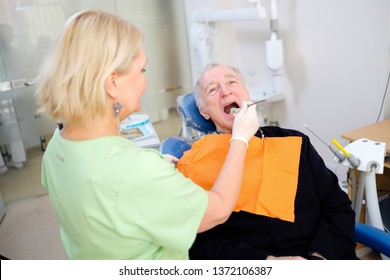 Blonde Woman Dentist Doing Dental Treatment Of Senior Male 70-75 Years Old Patient In Dental Clinic. Dental Care For Older People. Dentistry, Medicine And Health Care Concept