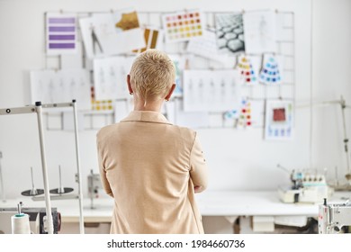 Blonde Woman Designer Beige Jacket Stands Near Sewing Equipment In Light Workshop