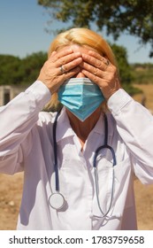 
Blonde Woman Doctor Wearing Surgical Mask On Eyes And Hands On Mouth Symbol Of Not Wanting To See Or Hear Or Talk About Negative Things About The Virus