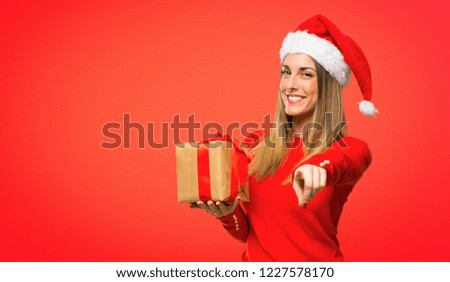 Blonde woman dressed up for christmas holidays points finger at you with a confident expression on red background