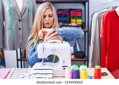 Blonde Woman Dressmaker Designer Using Sew Machine Checking The Time On Wrist Watch, Relaxed And Confident 