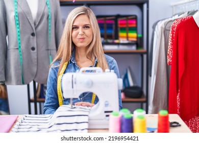 Blonde Woman Dressmaker Designer Using Sew Machine Puffing Cheeks With Funny Face. Mouth Inflated With Air, Crazy Expression. 