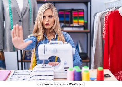 Blonde Woman Dressmaker Designer Using Sew Machine Doing Stop Gesture With Hands Palms, Angry And Frustration Expression 