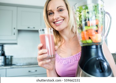 Blonde Woman Drinking A Smoothie In The Kitchen At Home