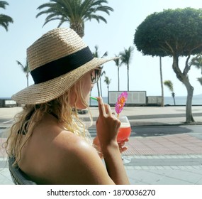 Blonde Woman Enjoying Her Cocktail At A Beach Bar On The Spanish Island Of Lanzarote. Sideview Of Blonde Girl With Hat And Cocktail.