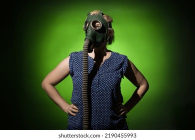 Blonde Woman In A Gas Mask Put Her Hands On Her Hips On A Dark Dramatic Background, Hard Light