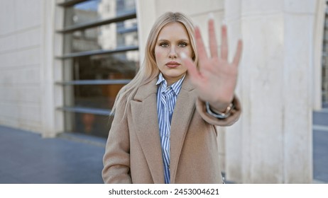 Blonde woman gesturing stop with hand in urban street setting, conveying boundaries and personal space message. - Powered by Shutterstock