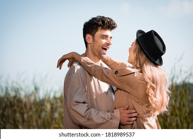 Blonde Woman In Hat Hugging Excited Man In Trench Coat