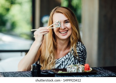 Blonde Woman Have A Sushi Time, She Holding Roll Under Her Eye. Funny Concept.