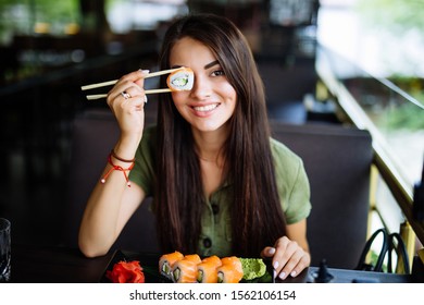 Blonde Woman Have A Sushi Time, She Holding Roll Under Her Eye. Funny Concept.