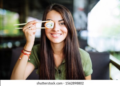 Blonde Woman Have A Sushi Time, She Holding Roll Under Her Eye. Funny Concept.