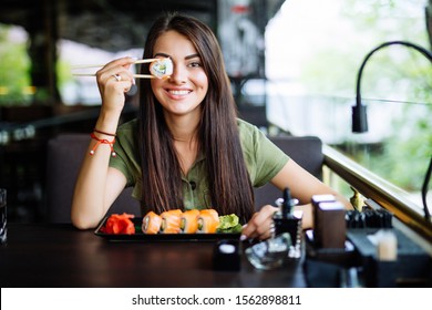 Blonde Woman Have A Sushi Time, She Holding Roll Under Her Eye. Funny Concept.