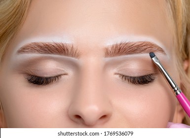 Blonde woman having permanent make-up tattoo on her eyebrows. Closeup beautician doing tattooing eyebrow. Green eyes close up. Professional makeup and cosmetology skin care.