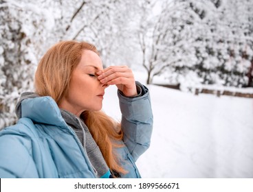 Blonde Woman holding her Nose outside in snowy winter day. Suffering from nasal sinus problems on cold weather.Copy space