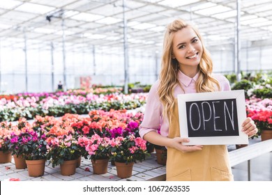 Blonde woman holding Open board by flowers in greenhouse - Powered by Shutterstock