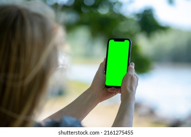 Blonde Woman Holding Phone With Empty Greenscreen And Taking Pictures Of Lake. Mobile Photography