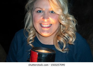 Blonde Woman Holds A Flashlight Under Her Chin, As If Telling A Ghost Story. Light Illuminates Face