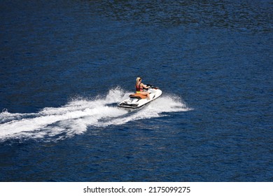 Blonde Woman In Life Vest Rides A Water Scooter On The Sea. Water Sport In Summer, Riding A Hydro Cycle