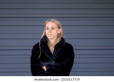 A blonde woman in a luxurious black fur coat stands with her arms crossed, looking off to the side with a thoughtful expression. - Powered by Shutterstock