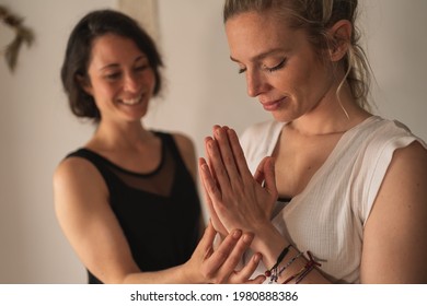 Blonde woman meditating with hands clasped next to her yoga instructor indoors