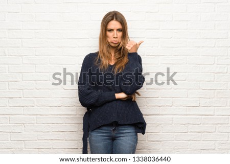 Blonde woman over brick wall unhappy and pointing to the side