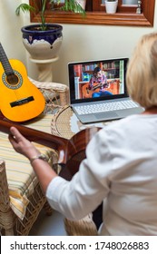 Blonde Woman Practicing Guitar With Online Video Class Using A Laptop At Home. Music Remote Class Or Online Tutorial. Technology And New Ways Of Learning.