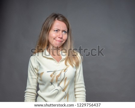 Blonde woman pulling funny face making an exaggerated grimace. Adult girl bulging eyes, pouts lips. Woman with awkward expressions of face has fun, plays fool. Portrait isolated on gray background