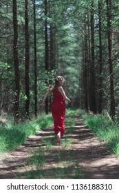 Blonde Woman In Red Dress Running Away From Camera On Forest Path.