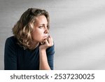 A blonde woman with short, wavy hair gazes thoughtfully to the side, resting their chin on their hand, against a plain background. Woman is sad and unmotivated, mental health awareness.