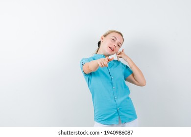  Blonde Woman Showing Phone Gesture, Pointing At Camera In Blue Blouse And Looking Merry , Front View. 