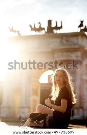 Blonde woman sits on the footstep before the Arch of Peace in Milan