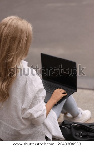 A blonde woman is sitting on the steps and working at her laptop.