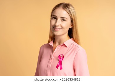 Blonde woman is smiling while wearing a pink ribbon pinned to her shirt to raise awareness about breast cancer - Powered by Shutterstock