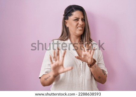 Blonde woman standing over pink background disgusted expression, displeased and fearful doing disgust face because aversion reaction. 
