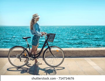 Blonde woman in summer hat with her bicycle walking coastline by the sea beach. Sea view. Freedom. Wind. Summer. Beach. Vacation. Looking to a sky and sea. Looking forward. - Powered by Shutterstock